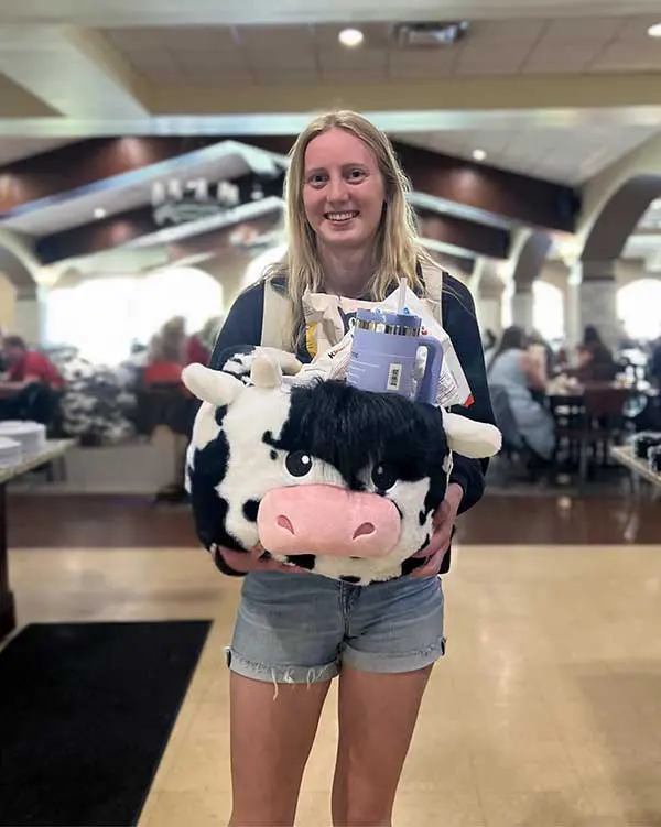 Student holding prize of stuff animal, insulated copy and snacks