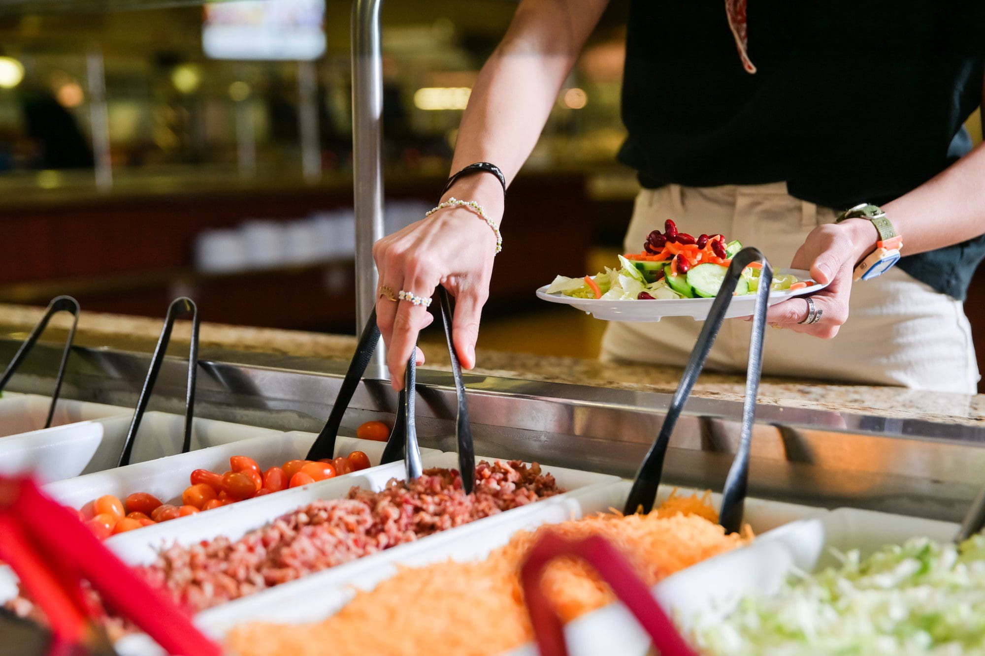 Hand using tongs at salad bar